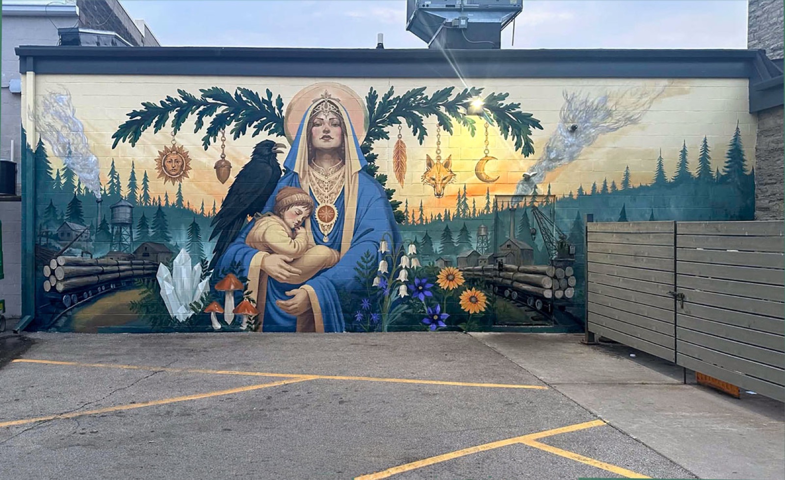Mill Madonnas mural, Oshkosh: a haloed madonna in blue robes holds a sleeping child beside a raven, framed by oak boughs, sun and moon charms, and twin lumber-mill scenes at dusk.